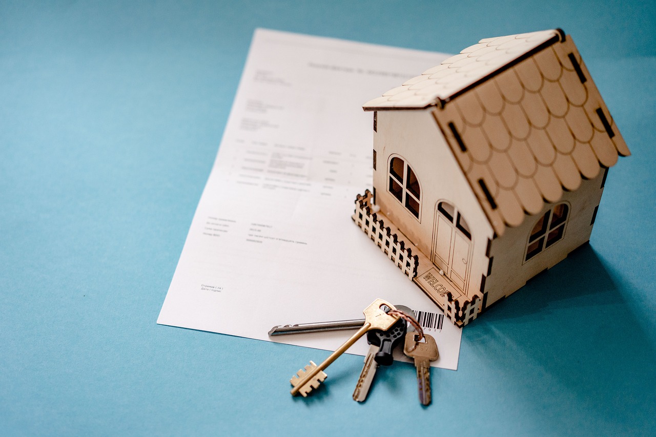 Imagem representando o direito imobiliário, mostrando uma casa de brinquedo, um molho de chaves e um contrato.